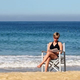 Eine Frau liest ein Buch am Meer