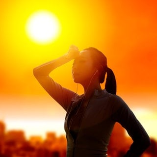 Eine Frau schützt in heißer Sonne ihre Augen: Hitzewellen sind belastend, doch mit der richtigen Anpassung lassen sie sich gut überstehen. Dazu gehört, sich nicht nur in klimatisierten Räumen zu schonen, sondern den Körper an Hitze zu gewöhnen.